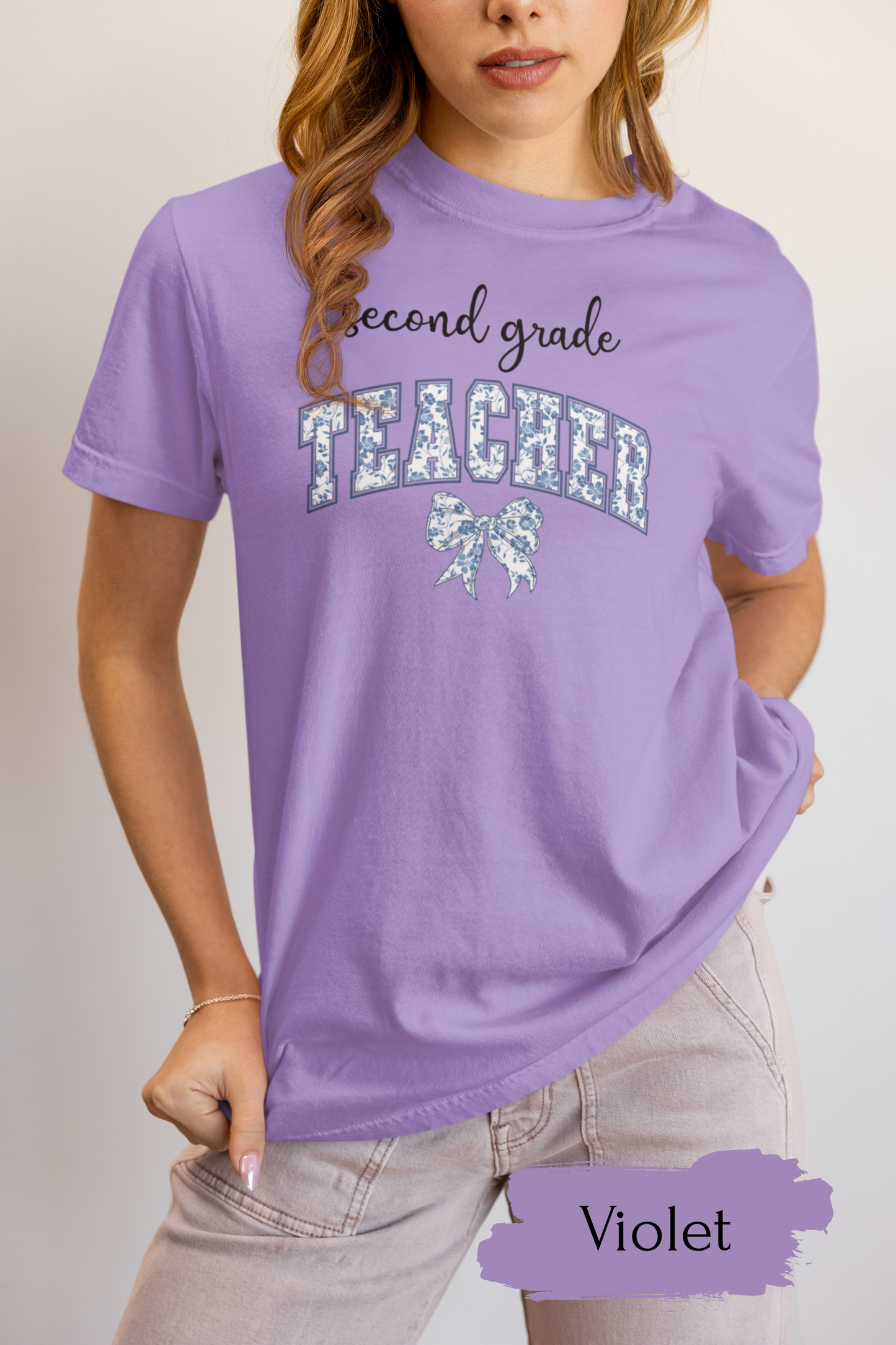 Person wearing a purple 'second grade teacher' t-shirt with decorative elements on a plain background.