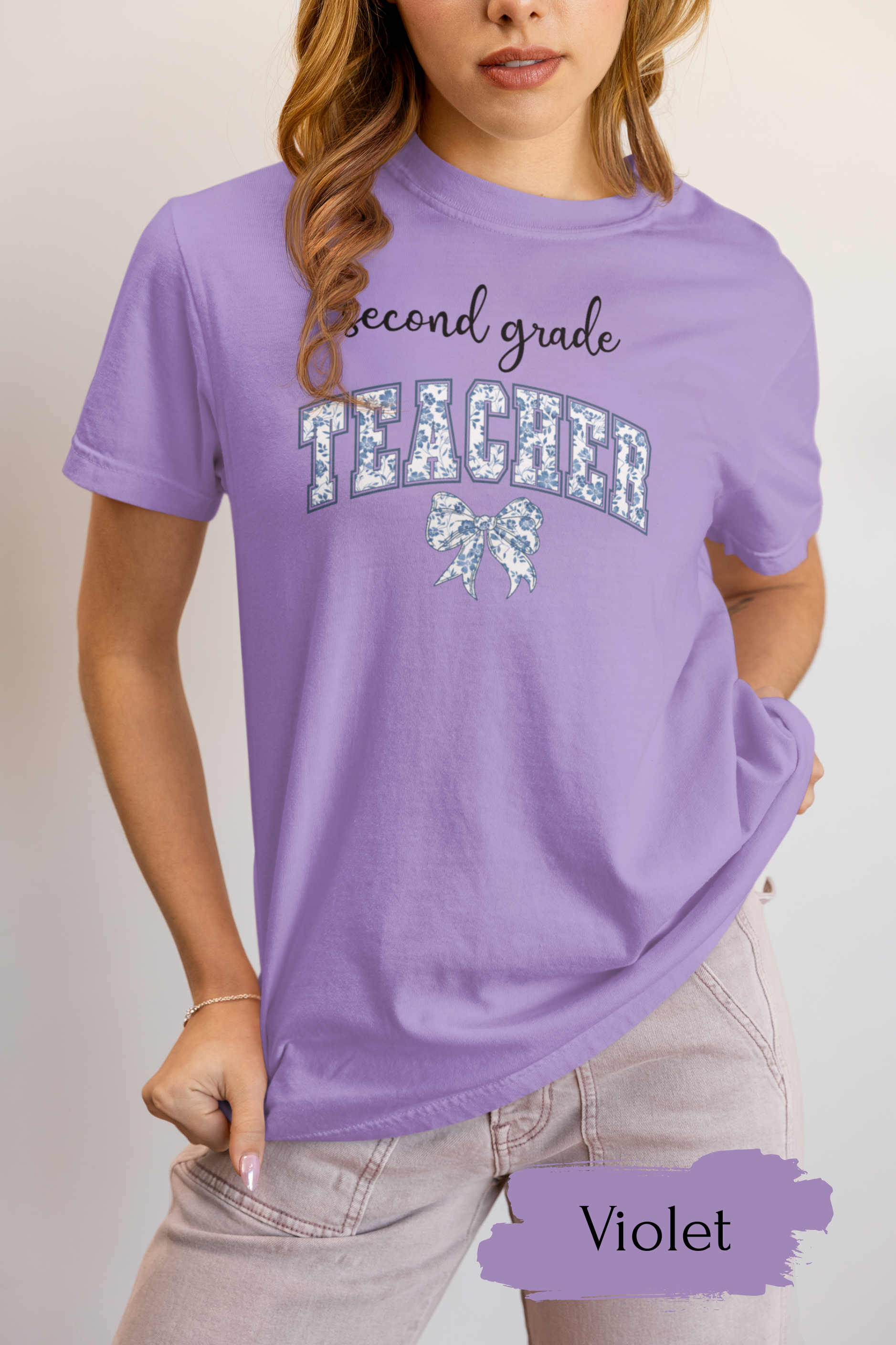 Person wearing a purple 'second grade teacher' t-shirt with decorative elements on a plain background.