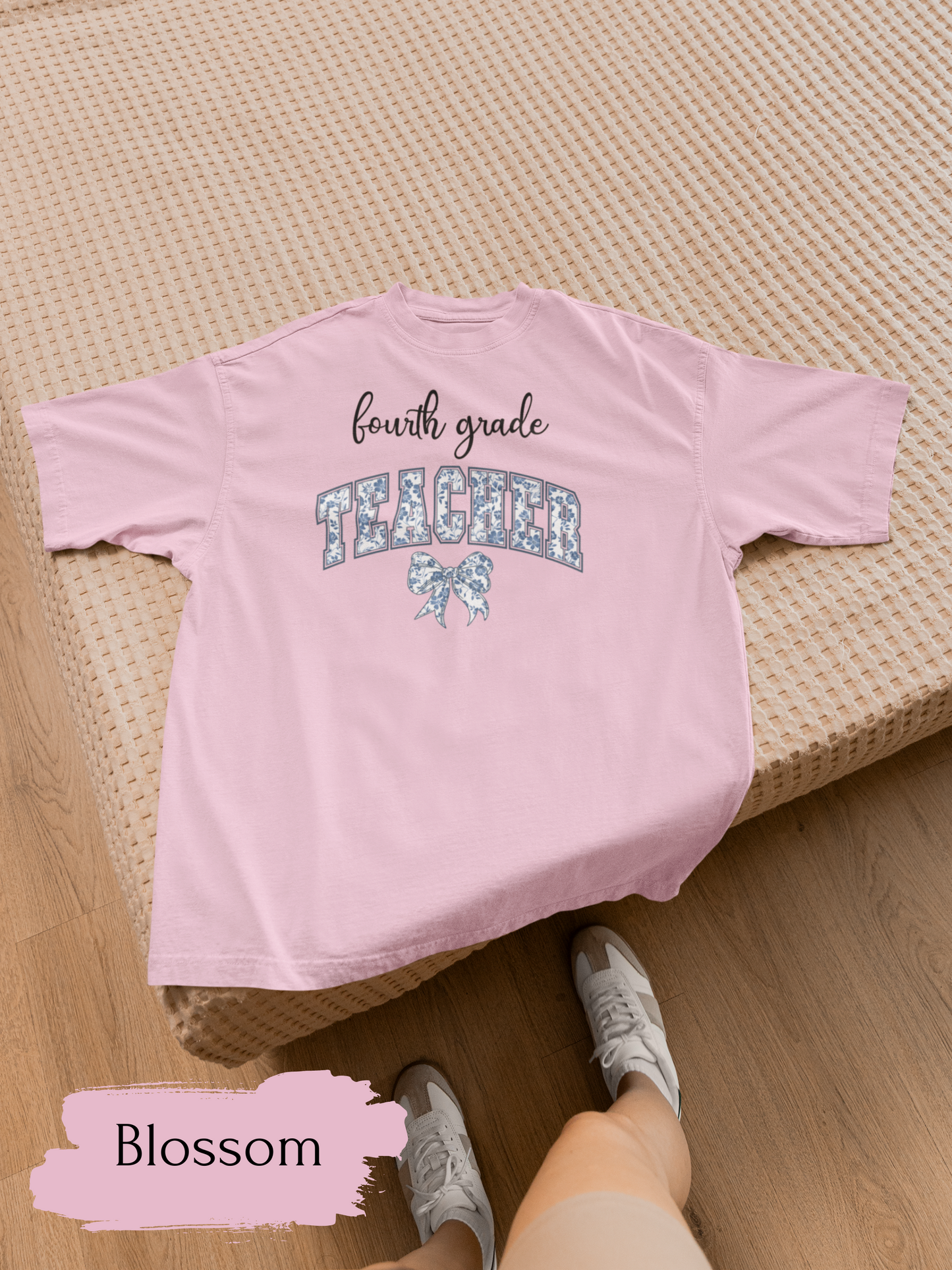 Pink t-shirt with 'fourth grade teacher' text on a woven surface